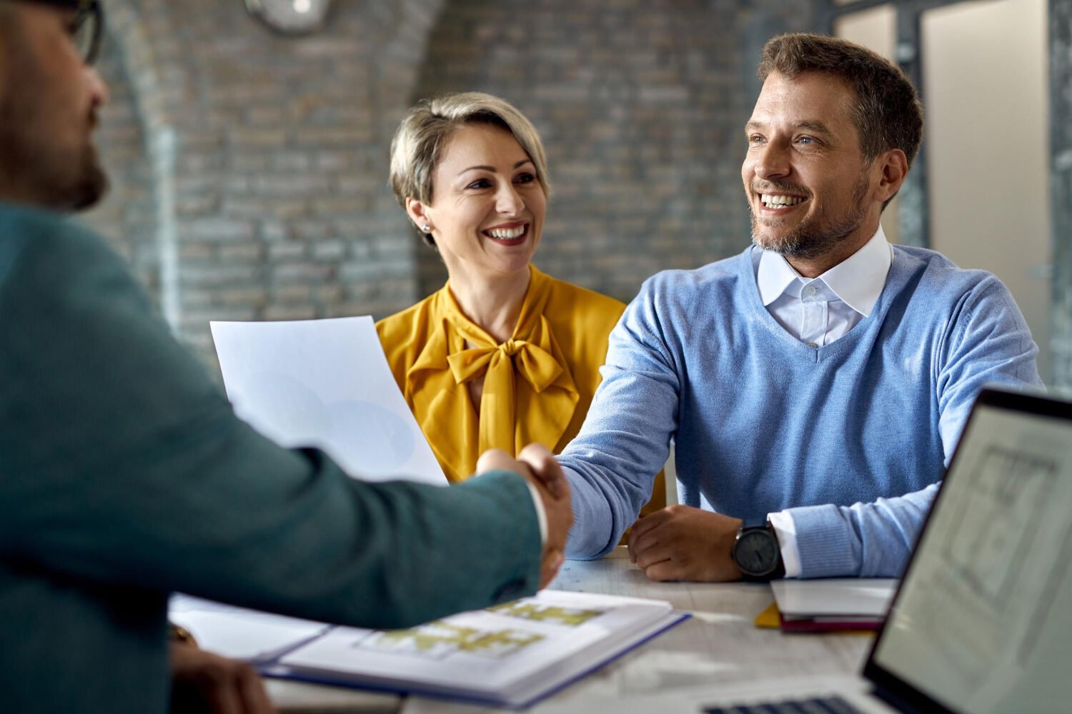 Poignée de main entre client et prestataire, personnages au second plan